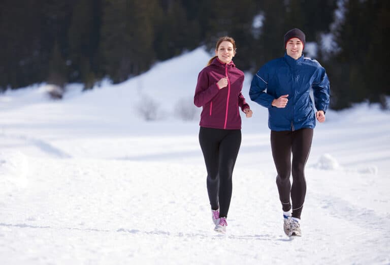 Jeune couple faisant du jogging sur la neige dans une forêt.